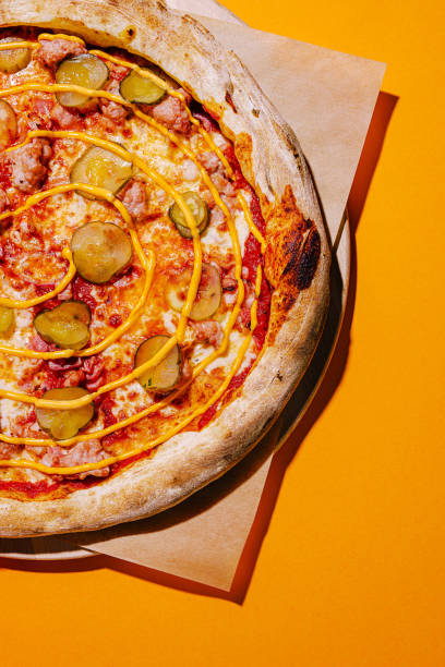 istock Unique pizza topped with cheese and pickles on a vibrant orange background 2200770377