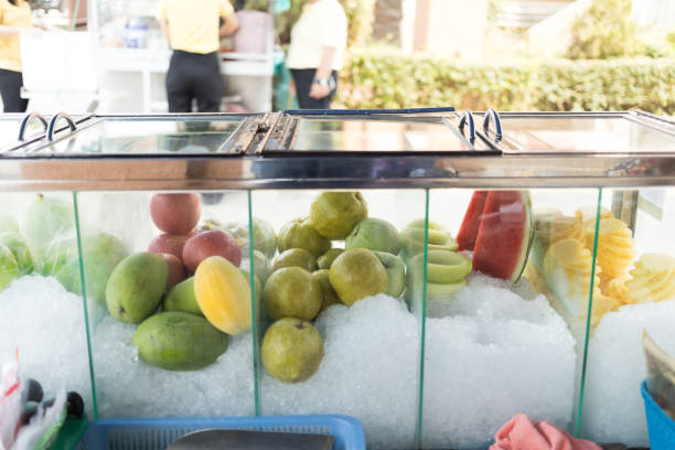 Frozen fruit trimmed ice in a glass cabinet for sale. Various fruits in the freezer of a food truck. Concept of a street food in Thailand