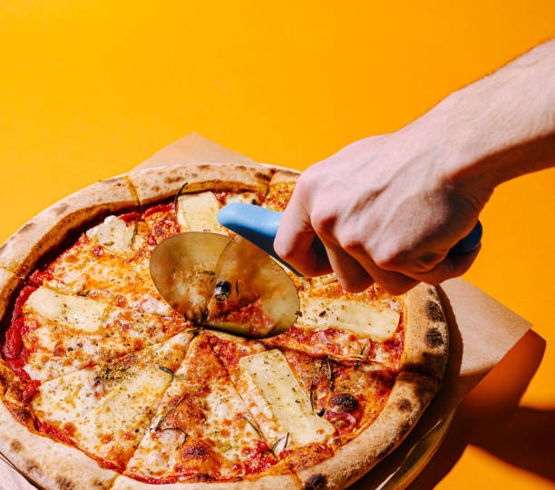 istock Delicious pizza being cut with a circular cutter on a vibrant yellow background 2200773615