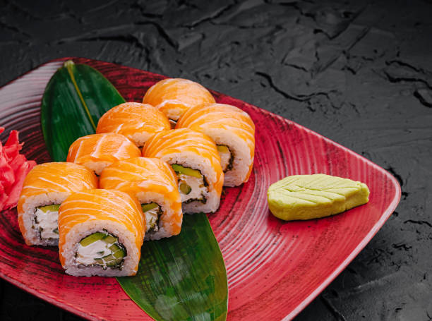 Colorful sushi rolls are arranged neatly on a vibrant red plate, accompanied by wasabi and garnished with pickled ginger.