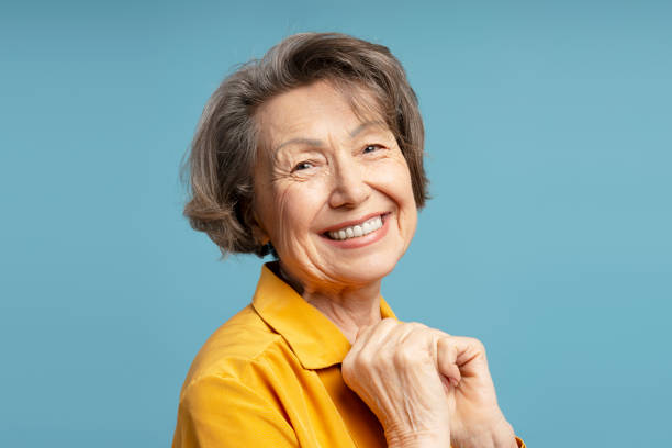 istock Happy senior woman smiling with clasped hands on blue background 2200774690