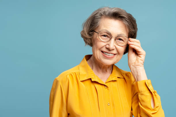 istock Smiling senior woman adjusting eyeglasses is posing in studio with blue background 2200774707