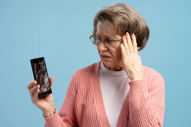 istock Senior woman holding broken smartphone with despair, touching forehead on blue background 2200775652