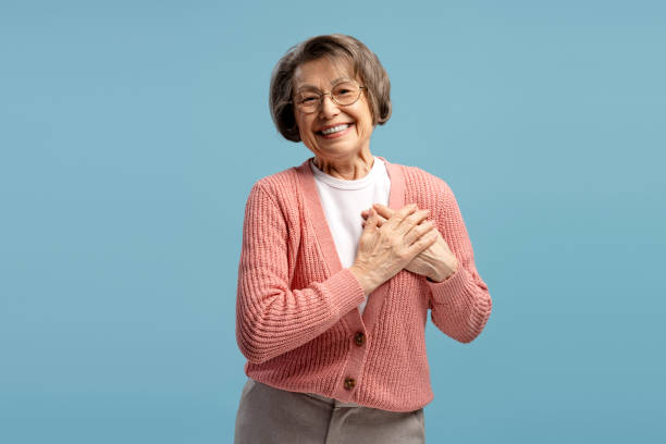 istock Grateful senior woman holding hands on chest smiling on blue background 2200775687