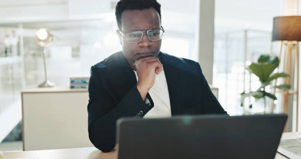 istock Laptop, thinking and businessman in office with reading, planning and ideas for online solution. Journalism, computer and African male editor with question, choice or decision for multimedia project. 2200778956