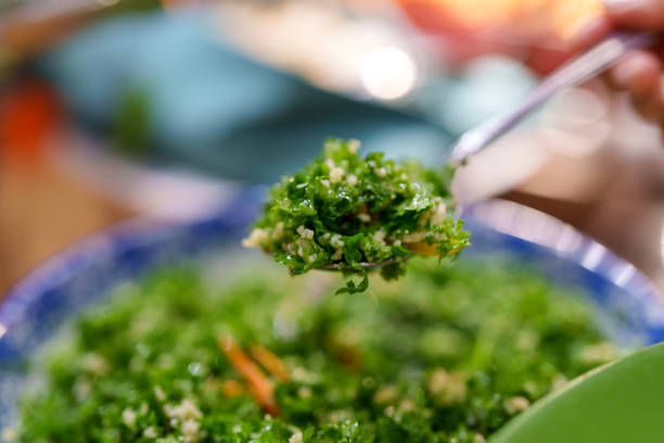 A person scooping fresh tabbouleh salad from a buffet selection, featuring parsley, bulgur, and vegetables in a Mediterranean-style setting.