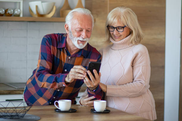 istock Senior couple using phone and reading online news while drinking coffee in the kitchen 2200785980