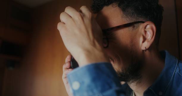A young man with glasses smiles while photographing indoors, close-up of his face