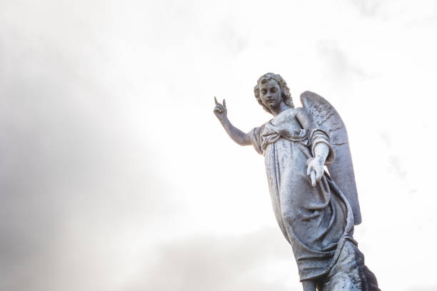 Dublin, Ireland - September 21, 2018: A towering angel statue with one hand raised stands against a dramatic cloudy sky in Glasnevin Cemetery, symbolizing peace and spirituality.