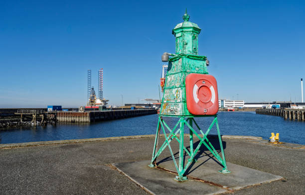 An industrial structure in vibrant green colors at a harbor with calm waters. Industrial installations and a clear blue sky in the background accentuate the maritime and industrial ambiance.