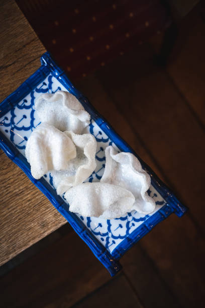 Close-up of crispy prawn crackers served on a traditional blue and white ceramic plate, placed on a rustic wooden table, Authentic Asian appetizer and snack food photography concept