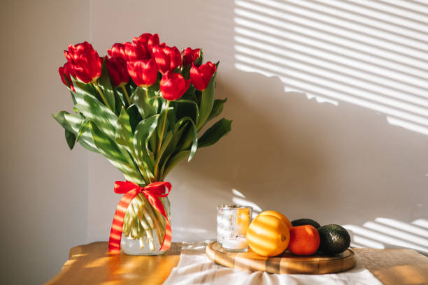 A stunning red tulip sits elegantly on a table, bathed in soft morning light. Home decor