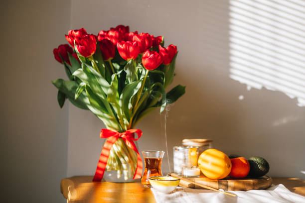 A serene scene of lighting and smelling joss sticks, with a soft focus on a floral arrangement in the background