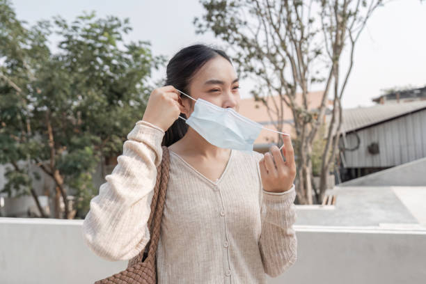 istock Young woman removing her mask while smiling outdoors in a public space. 2200794784