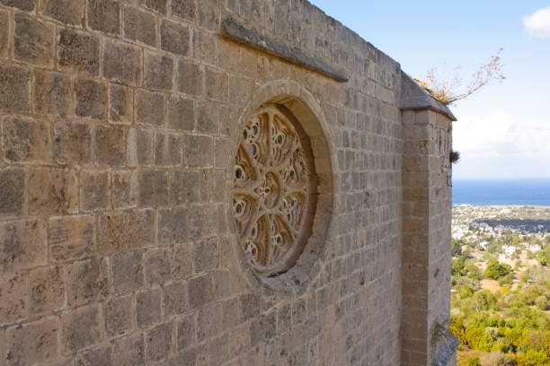 Stone wall with circular window and blue sky and city in background, medieval structure
