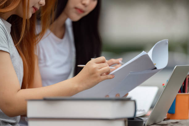 istock Diverse university students reviewing papers and taking notes outdoors with a laptop. 2200798502