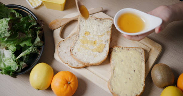 High angle view, Woman's hands pouring honey on whole wheat bread on wooden cutting board in kitchen. Food preparation.