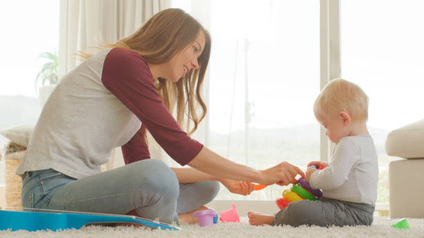 istock Mother Sits With Baby Son At Home Playing With Plastic Stacking Toys 2200799260