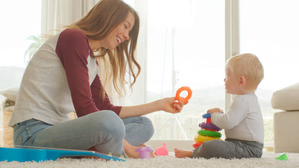 istock Mother Sits With Baby Son At Home Playing With Plastic Stacking Toys 2200800561