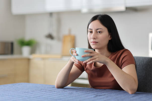 istock Distracted asian woman drinking coffee in the kitchen 2200802302