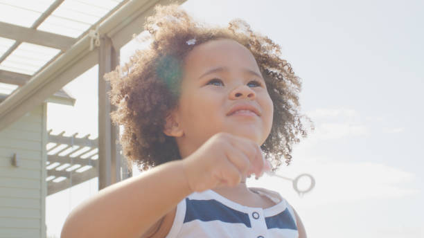 istock Excited Young Girl Having Fun Sitting Outside Blowing Bubbles 2200802480