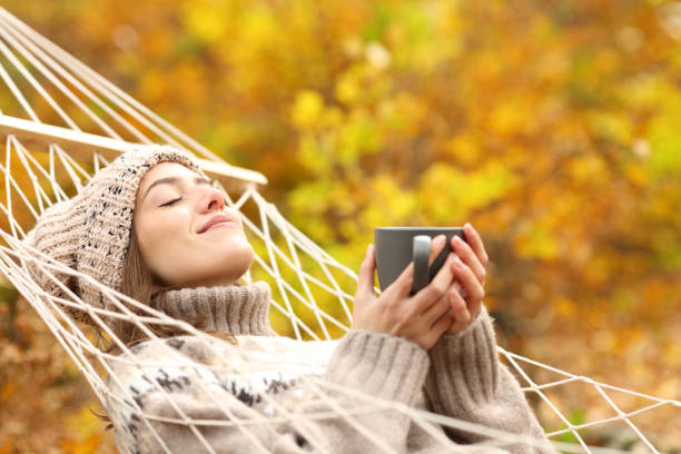 Satisfied woman drinking and resting on hammock in autumn