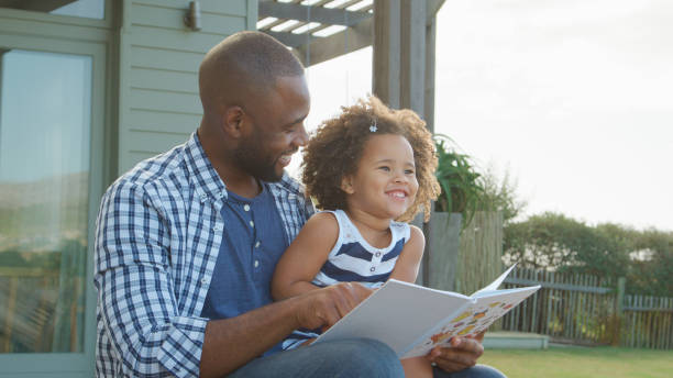 istock Father Sitting With Daughter Outside Reading Book Together 2200803149