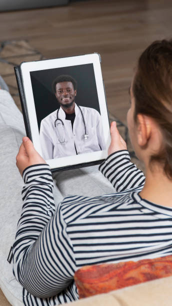 istock Woman Lying On A Sofa And Talking With A African Doctor Online Using Digital Tablet. Telemedicine Concept. 2200805906