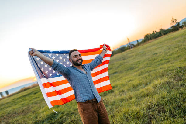 istock Young Man Holding Up A USA Flag While Standing In The Field At Sunset 2200806303