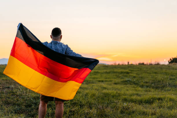 istock Rear-View Of A Young Man Holding Up A German Flag While Standing In The Field At Sunset 2200807004