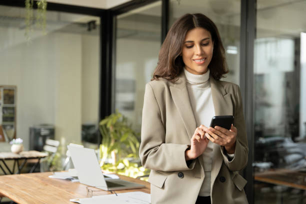istock Middle aged Hispanic business manager ceo using cell phone mobile app, laptop. Smiling Latin or Indian mature woman businesswoman holding smartphone sit in office working online on gadget, copy space. 2200807110