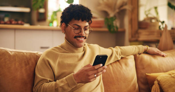 istock Smartphone, young man and mobile app in home with smile, texting or communication on couch for relax. Male person, positive and happy on technology in apartment for post, online and website in lounge 2200807129