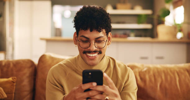 istock Smartphone, young man and mobile app with smile, texting or communication on couch in home for relax. Male person, positive and happy on technology in apartment for post, online and website in lounge 2200807184