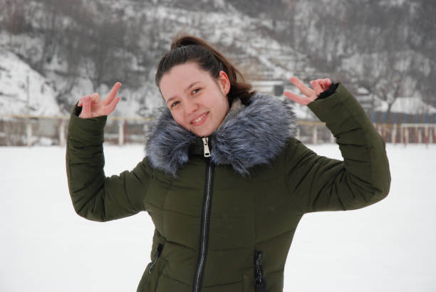 The cheerful woman crates funny poses on the magic snowfall in winter