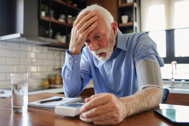 istock An elderly man with grey hair and a beard sits in his home kitchen, looking unwell and frightened while checking his blood pressure on a digital monitor. He appears concerned or sick, reacting to the results 2200813092
