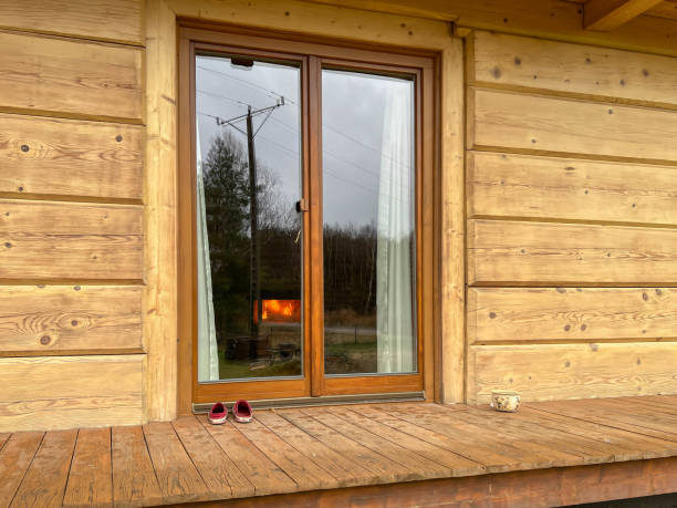 A veranda window in a wooden log house visible from the outside. Inside, a fireplace flame visible.