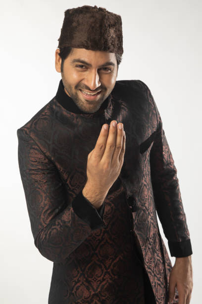 Portrait of smiling mid adult groom dressed in kurta and skull cap greeting adab while standing against white background