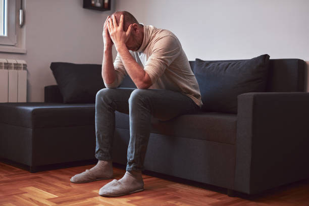 istock Man with headache and depression sitting on a sofa at home. 2200828452
