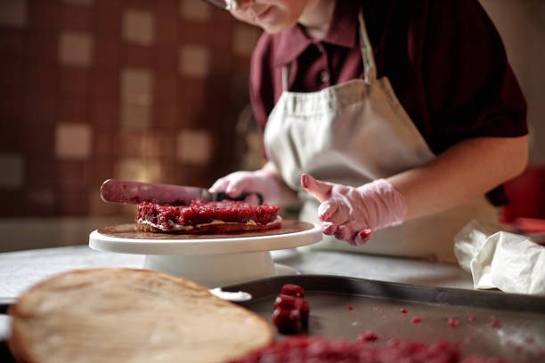 istock Female Chef Covering Cake Layer with Cherry Jam Making Craft Pastry in Confectionery Kitchen 2200829800