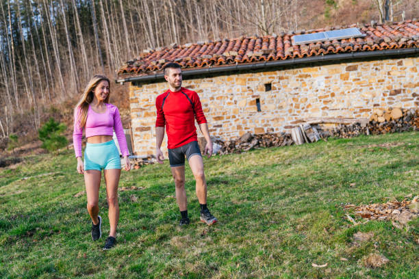 Young couple walking on grass in sportswear in front of a stone house with a solar panel on the roof