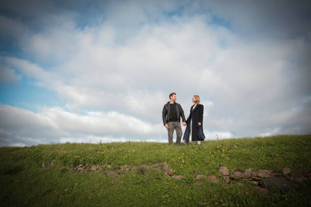 istock Happy couple holding hands on green hill under cloudy sky 2200831212