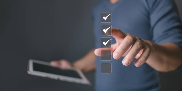 istock Businessman holding tablet and tapping checkbox, selecting online digital form for audit, quality control, voting, survey and evaluation with business success. 2200833390