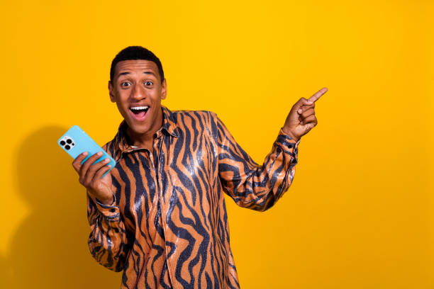 istock Excited young man holding phone points to the side with a vibrant yellow background 2200835162