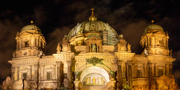 Berlin, Germany – January 3, 2025: The iconic Berlin Cathedral (Berliner Dom) beautifully illuminated at night during a winter evening. The historic Protestant church, located on Museum Island, showcases its stunning Baroque and Neo-Renaissance architecture against a dramatic dark sky. The golden lighting highlights the intricate details of the cathedral’s domes, statues, and facade, creating a captivating scene in the heart of Berlin.