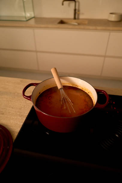 Red pot filled with soup and a whisk on a stove in a modern kitchen setting
