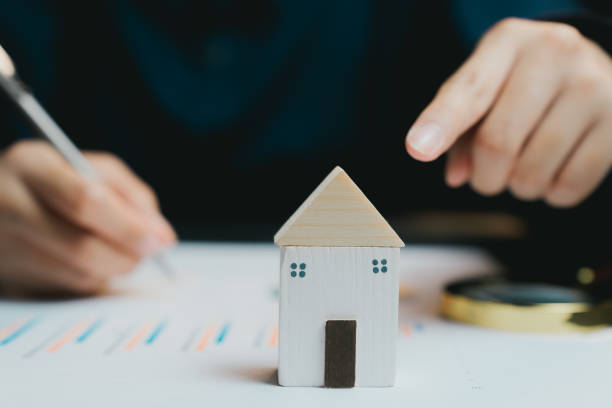 istock Wooden Model House on Table with Person Pointing to Document 2200848746