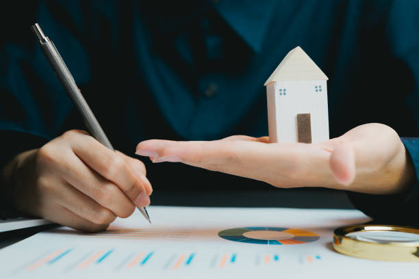 istock Hand Holding Miniature House Model on Table with Financial Documents 2200848747
