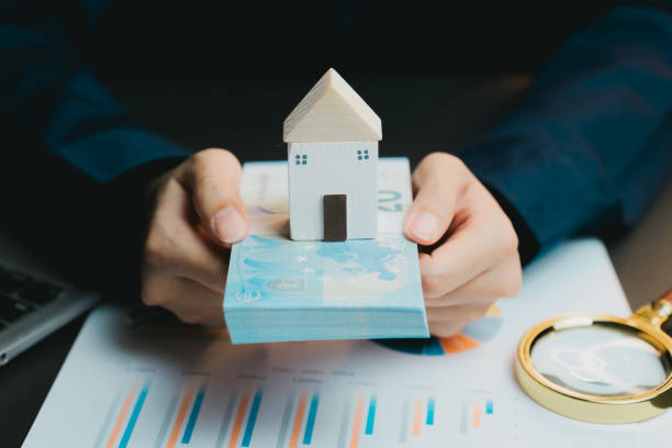 istock Hands Holding Wooden House Model on Stack of Money and Documents 2200848759