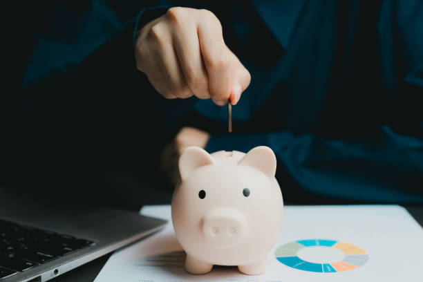 istock Person Inserting Coin Into Piggy Bank on Financial Documents 2200848778