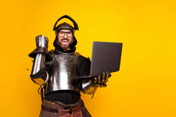 istock Knight in medieval armor excitedly using a laptop against a yellow background 2200850834